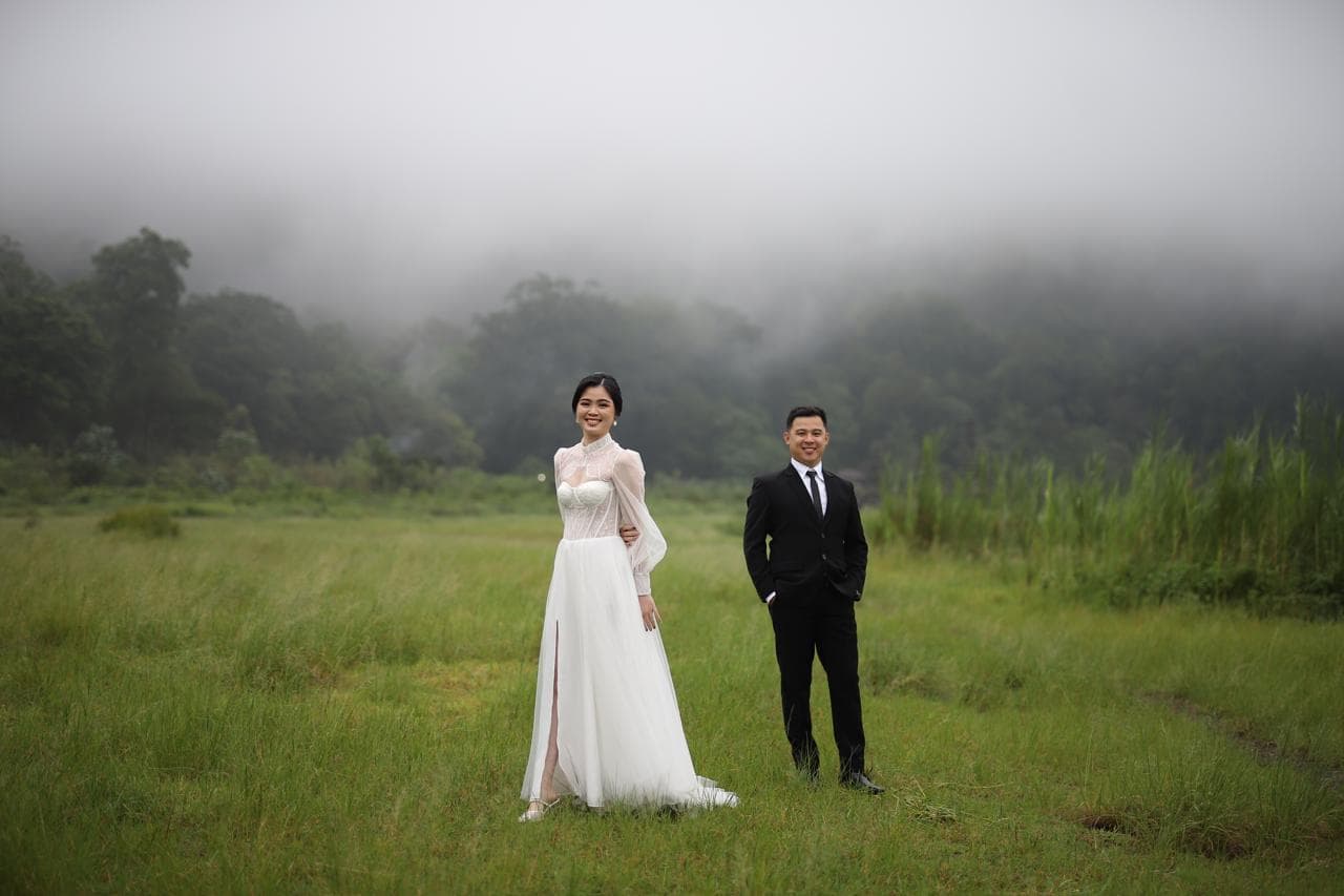 Bride and groom standing together in an open meadow.