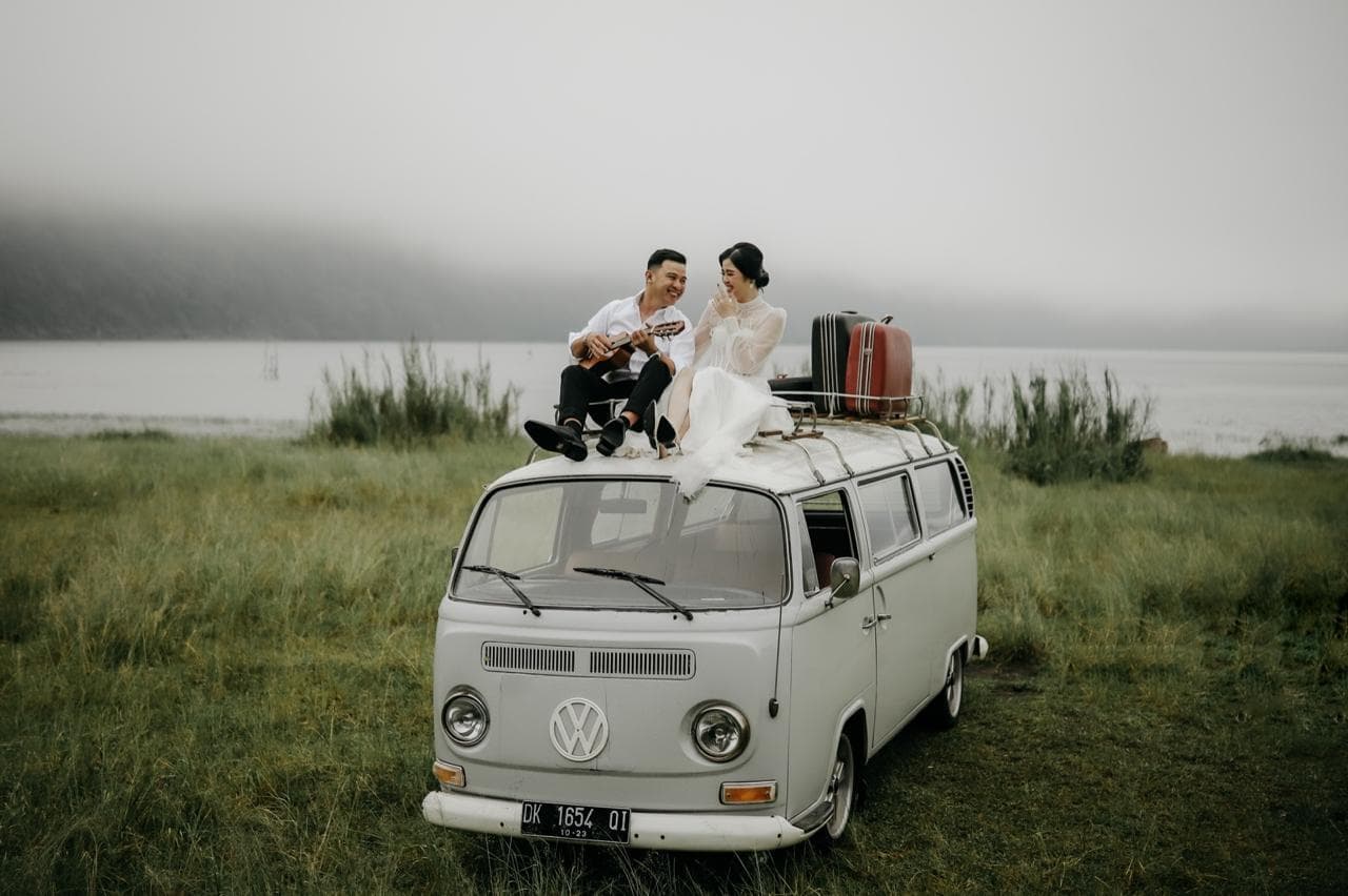 Newlyweds sitting on a vintage van outdoors.